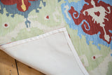 Textured Indian Chainstitch rug showing backing and vibrant Ikat pattern in blue, red, green, ivory.