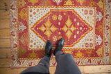 Vintage Oushak rug with red field, geometric motifs, and black boots.