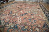 Vintage Heriz carpet's faded cinnabar red field, scrolling serrated leaves and dark blue border.