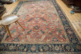 Blanched Heriz carpet corner view: dark blue border, faded red field, scrolling serrated leaves.