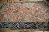 Vintage Heriz carpet: navy geometric border, blush field, and visible knot head wear.