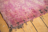 Vintage Moroccan carpet with plush cranberry mauve pile, dark motifs, and tattered fringe.