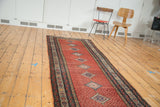 Elongated distressed Malayer runner with faded cherry red field and geometric medallions.
