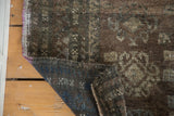 Distressed Oushak rug fold, showing textured brown pile, mauve selvage, and blue geometric foundation.
