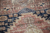Distressed pile of Oushak rug showing navy, blush, and ivory geometric florals.