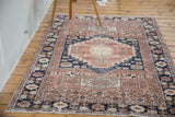 Distressed blush rose and navy Oushak rug corner, featuring geometric floral border and ivory fringe.