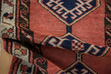Folded vintage Sarab runner, thick pile, faded brick red field, and navy geometric medallion.