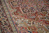 Close-up of vintage Heriz carpet's serrated stepped spandrels in brick red, navy, and ivory tones.