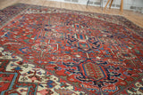 Vintage Heriz carpet corner detail, displaying traditional geometric patterns in brick red, navy, and cream tones.