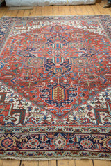 Traditional geometric Heriz carpet corner with red, navy, aqua motifs and textured fringe.