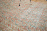Angled view of distressed Turkish Oushak rug, showing faded cinnabar and teal paisley boteh motifs.