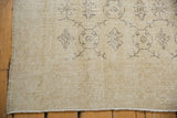 Distressed Turkish Oushak rug corner, blanched ivory field, minimalist charcoal vinery.