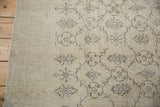 Distressed charcoal vinery and floral on blanched ivory Oushak, showing secured edge.