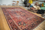 Distressed Ahar Heriz carpet featuring cherry red field, navy borders, and artfully faded patterns.