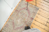 Distressed Oushak rug: faded mint floral medallion, violet hexagonal border, and worn edge.