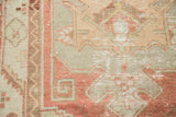 Localized distress and tribal geometric pattern in celadon and cinnabar on Oushak rug.