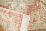 Folded edge of a distressed Oushak rug, showing plain weave, braided fringe, and low pile texture.