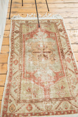 Distressed Oushak rug corner with tribal motifs, faded cinnabar, subdued celadon, and fringe.