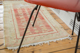 Faded cherry red and sand abrashes on distressed Oushak rug end with tattered fringe.