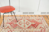 Distressed Oushak rug corner with tribal geometric medallion in faded red and ivory.