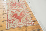Distressed Oushak rug corner, faded cherry red geometric tribal pattern, emerging arrows, ivory fringe.