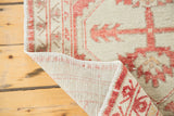 Curled edge of a distressed Oushak rug, showcasing faded cherry red tribal motifs and woven back.