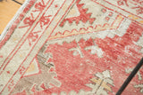 Textured distressed pile of vintage Oushak rug with faded red, ivory, and sand geometric patterns.