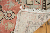 Distressed Oushak rug's blush-toned pile, white fringe, and hand-knotted foundation.