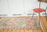 Distressed Turkish Oushak rug with faded cranberry red field, geometric floral motifs, and varied texture.