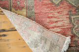 Curled corner of distressed Oushak rug reveals hand-knotted foundation, faded cranberry pile, and white fringe.