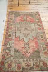 Distressed Oushak rug corner showing geometric floral motifs and faded cranberry field.