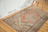 Distressed Oushak rug corner with faded cinnabar red, grey, and beige geometric patterns.