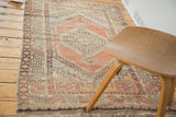 Faded cinnabar red and grey geometric medallion with hooked character, distressed texture, and fringe.
