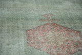 Distressed Oushak carpet, faded blush herati diamond motif on muted green field.