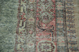Distressed vintage Oushak rug showing faded green, blush rose, and beige stylized motifs.