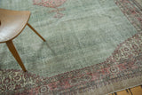 Corner of distressed Oushak carpet showing blush floral border and soft green field.