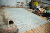 Distressed Turkish Oushak carpet partially unrolled, showing faded aqua and rose colors.