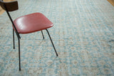 Angled view of distressed Oushak carpet with faded aqua field and wooded patterns.