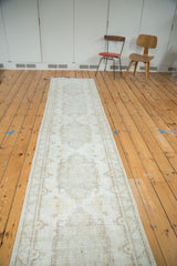 Distressed Oushak runner with faded ivory medallions and beige border patterns.