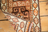 Curled corner of vintage Oushak rug displaying 'HASAM' text and hexagonal serpent border.