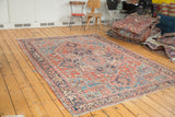 Distressed vintage Heriz carpet, featuring brick red field with vivid blue and green tendril patterns.