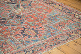 Distressed vintage Persian Heriz rug close-up, displaying brick red, sky blue, and navy geometric floral motifs.