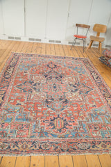 Distressed Heriz rug corner with vivid brick red field, intricate blue geometric spandrel, and patterned border.