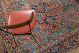 Distressed Heriz carpet's rich brick red pile with blue and green geometric floral patterns.
