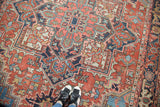 Distressed Heriz carpet close-up: faded brick red field, geometric motifs, and sky blue accents.