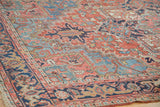 Textured brick red field with blue geometric patterns on a distressed Heriz carpet.
