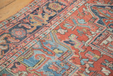 Close-up of distressed brick red Heriz rug with blue, gold, and peach floral tendrils.