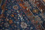 Vintage Shiraz carpet detail with stylized human figure, tribal motifs, indigo, red, and orange.
