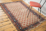 Corner of a distressed Malayer rug featuring an indigo blue border and aged fringe.