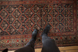 Distressed Kurdish rug detail: charcoal field, serrated diamond lattice, floral motifs in brick red.